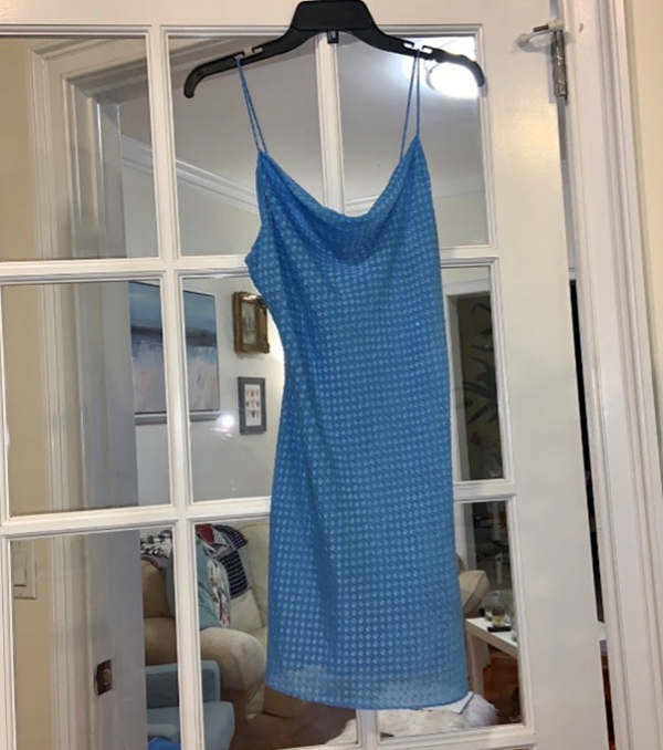 Blue slip dress hanging on a hanger in front of a glass-paneled door.
