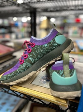 Colorful running shoe with teal and purple panels, pink laces, displayed on a shelf in a retail store.
