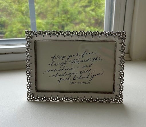 Ornate beaded frame on a windowsill holding a handwritten quote.