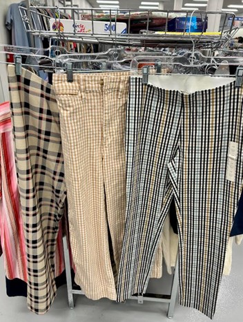 Row of plaid and checked pants hanging on a clothing rack in a store.