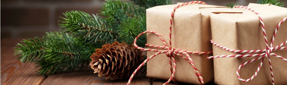 Brown kraft-wrapped gifts tied with red-and-white twine, beside pine branches and a pine cone on a wooden surface.