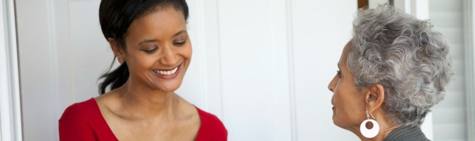 Young woman in a red top smiling at an older woman with gray hair and large circular earrings.
