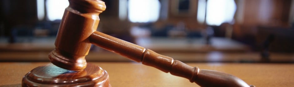 Wooden gavel resting on a courtroom desk with blurred benches in the background.