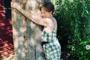Woman leaning against a tree outdoors, wearing a green patterned dress.