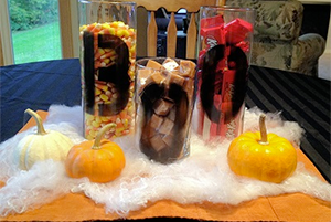 Halloween-themed candy display on a table with treat bags, small pumpkins, and fake cobwebs.