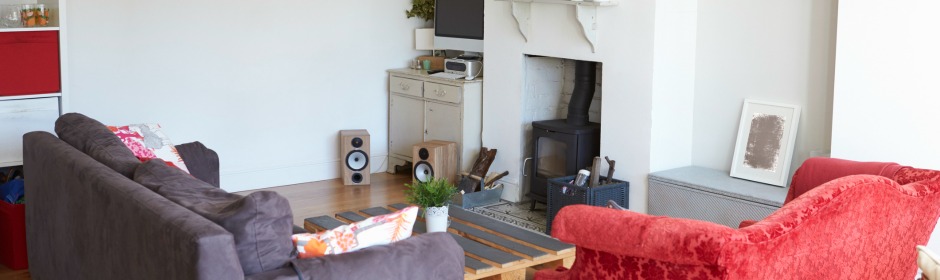 Cozy living room with a wood-burning stove, gray sofa, red armchair, and a wooden coffee table.