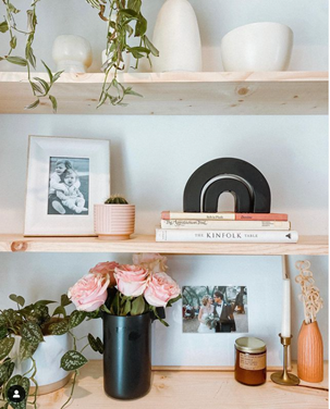 Shelf decor featuring plants, vases, a framed photo, books, and pink roses in a dark vase.