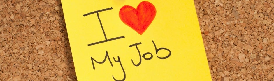 Yellow sticky note on a corkboard reading I love my job with a red heart.