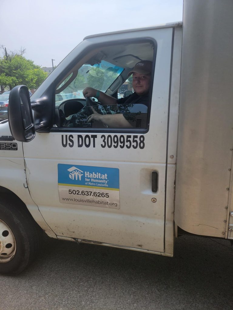 White delivery van with Habitat for Humanity sticker, driver inside cab.