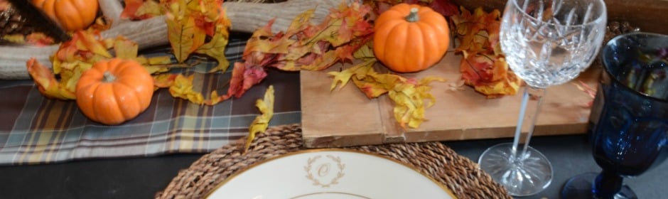 Autumn table setting with small pumpkins, colorful leaves, and glassware on a plaid table runner