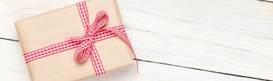 A brown paper-wrapped gift tied with a red and white gingham ribbon on a white wooden surface.