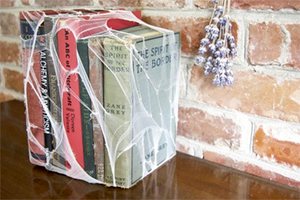 Decorative cube wrapped in colorful book spines tied with string on a wooden table beside a lavender sprig.