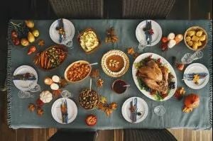 Top-down view of a festive table with a roasted turkey, pies, and bowls of sides on a blue tablecloth.