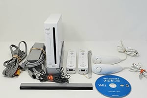 Nintendo Wii console with two motion remotes, sensor bar, cables, and a blue disc on a white surface.