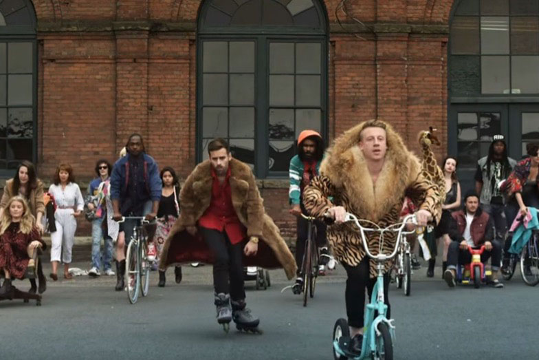 People in oversized fur coats skating and riding bicycles in a city street parade.