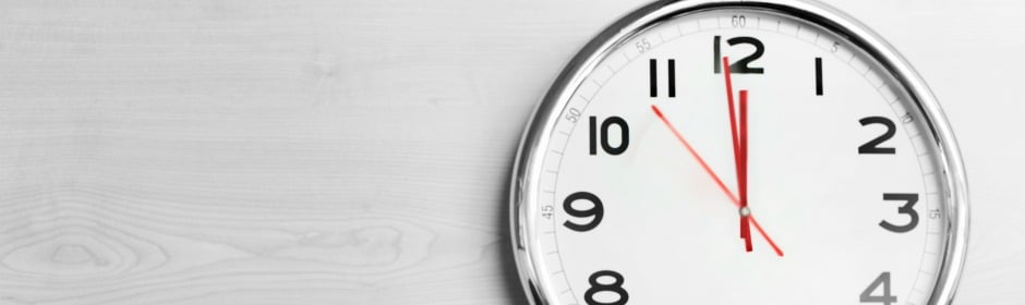 Round analog clock with red hands on a light wooden surface