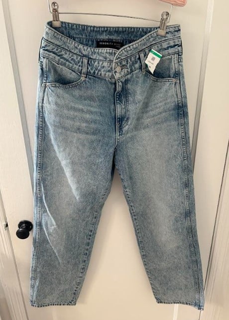 Light-wash denim jeans hanging on a metal hanger against a white door.