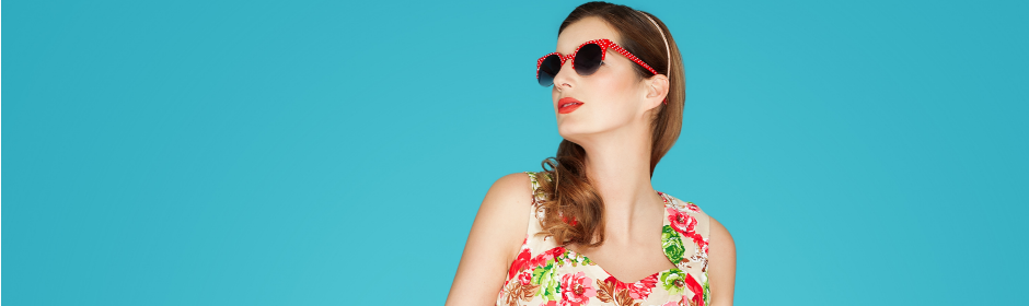 Woman wearing a floral dress and red sunglasses against a turquoise background.