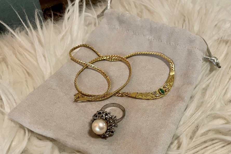 Gold rope bracelet, an engraved gold bracelet with a green stone, and a pearl ring displayed on beige fabric.