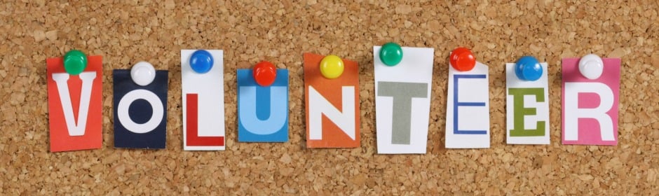 Colorful letters pinned on a corkboard spell 'VOLUNTEER' with multicolored pins.