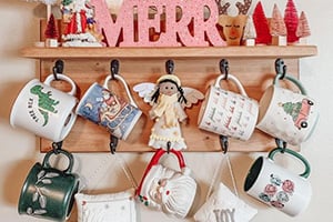 Wooden mug rack with hanging Christmas mugs, a doll in a red dress, and decorative trees under a MERRY sign.