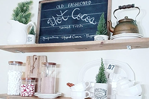 Shelf with glass jars, a kettle, a chalkboard sign, and small potted plants in a bright kitchen.