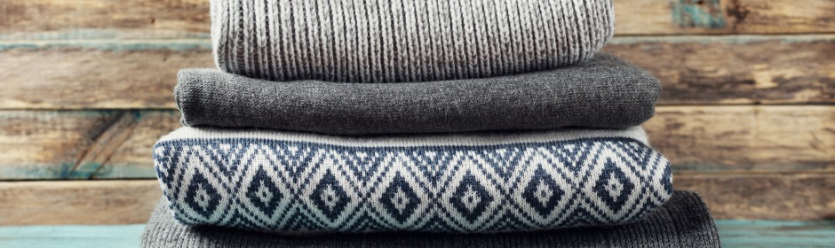 Stack of folded sweaters in varying gray tones on a rustic wooden surface.