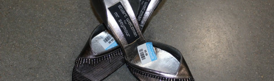 Crossed black sandals with price tags on a gray floor.