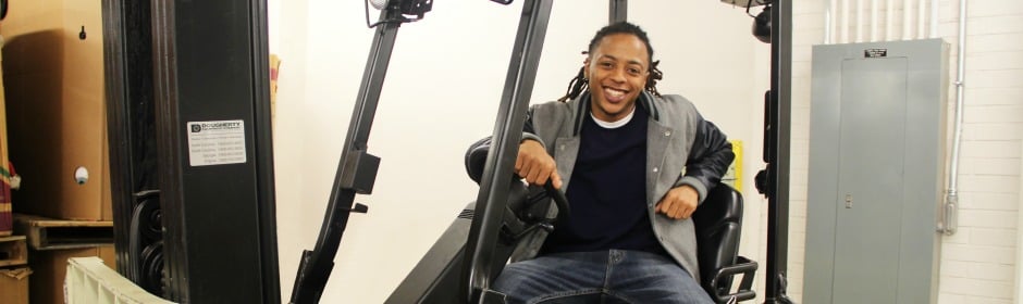 Smiling man seated in a forklift cab inside a warehouse