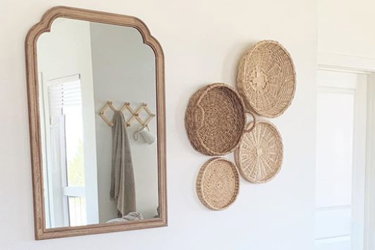wall decor featuring a wooden-framed mirror on the left and five round woven wicker baskets arranged in a cluster.
