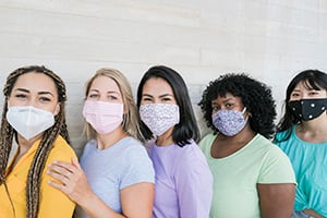 Five diverse people stand in a row wearing colorful shirts and face masks.