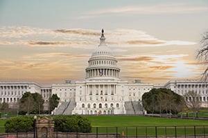 Capitol building in Washington, DC at sunset with green lawn and trees in the foreground