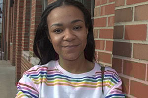 Smiling young woman in a striped shirt standing beside a brick wall.