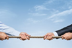 Two people pull a rope in a tug-of-war against a clear blue sky.
