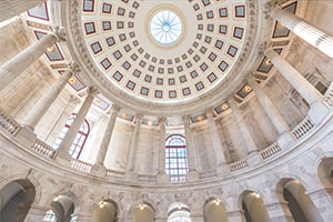 Interior view of a grand domed rotunda with a circular skylight, tall marble columns, and arches.