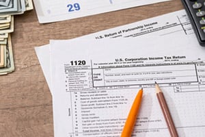 Tax forms on a wooden desk with a pencil, calculator, and cash in the background