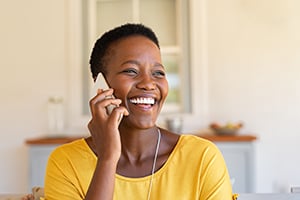 Smiling woman on a phone call indoors, wearing a bright yellow top.