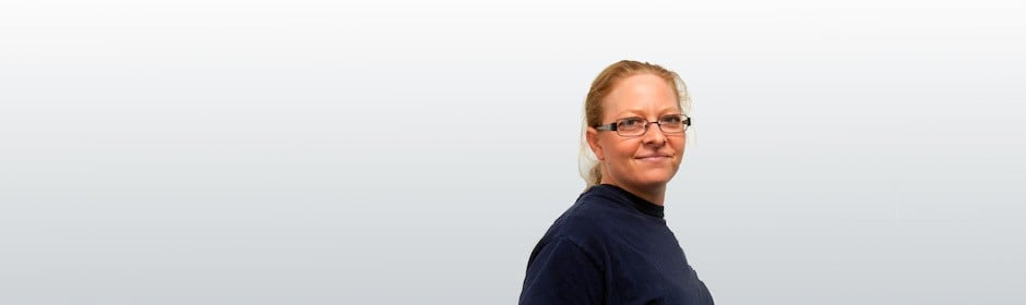 Portrait of a woman with glasses wearing a navy sweater, angled slightly to the right against a pale gradient background.