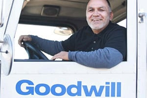 Smiling man sits in the cab of a white Goodwill truck with the logo on the door.