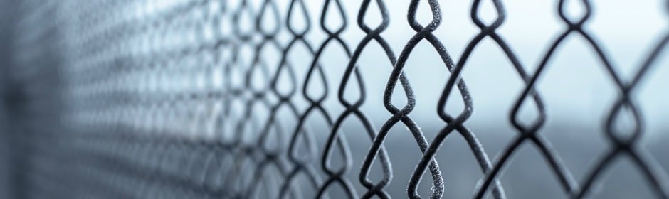 Close-up of a chain-link fence with frost on the wires and a soft, blurred background.