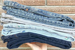 Stack of folded denim jeans in various washes held against a brick wall.