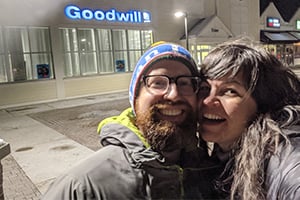 Smiling two people taking a selfie outside a Goodwill store at night.