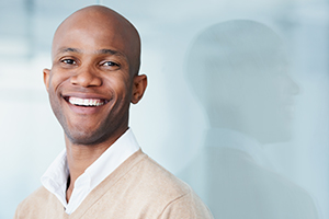 Smiling bald man in a light beige sweater and white shirt in an office setting