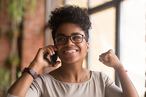 Smiling woman with short curly hair and glasses talking on a smartphone indoors