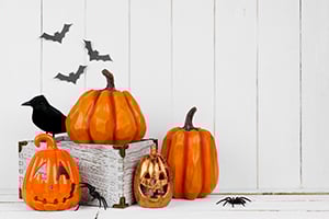 Carved jack-o'-lanterns and hanging bats arranged on a white wooden surface for Halloween.