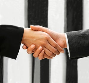 Close-up of a handshake between two professionals in suits against a striped background.