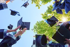 Graduates celebrate by tossing mortarboards into the air under a clear blue sky.