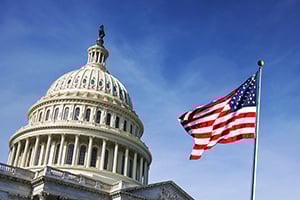 U.S. Capitol dome with a waving American flag against a clear blue sky