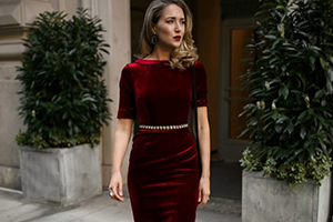 Woman in a burgundy velvet dress standing outside a doorway with potted greenery.