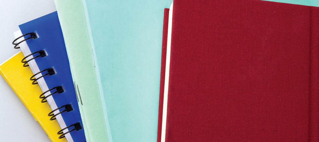 Stack of colorful spiral-bound notebooks and binders arranged diagonally, with a red hardcover book on the right.